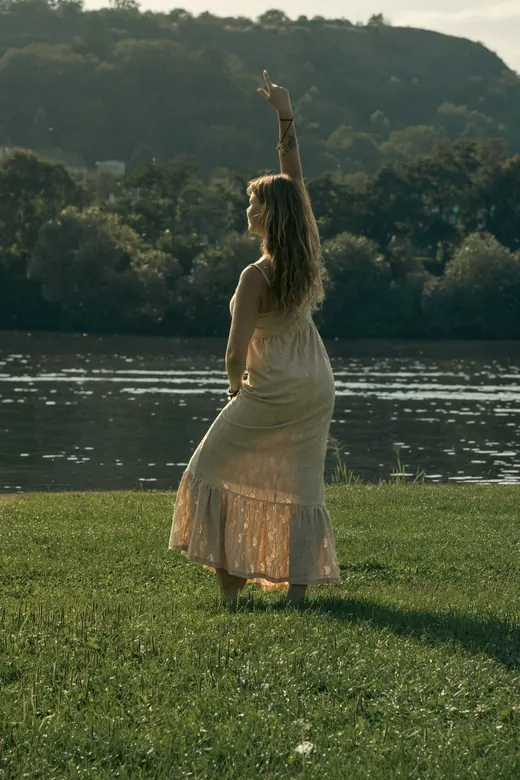 Rezi with arms raised by the river at golden hour